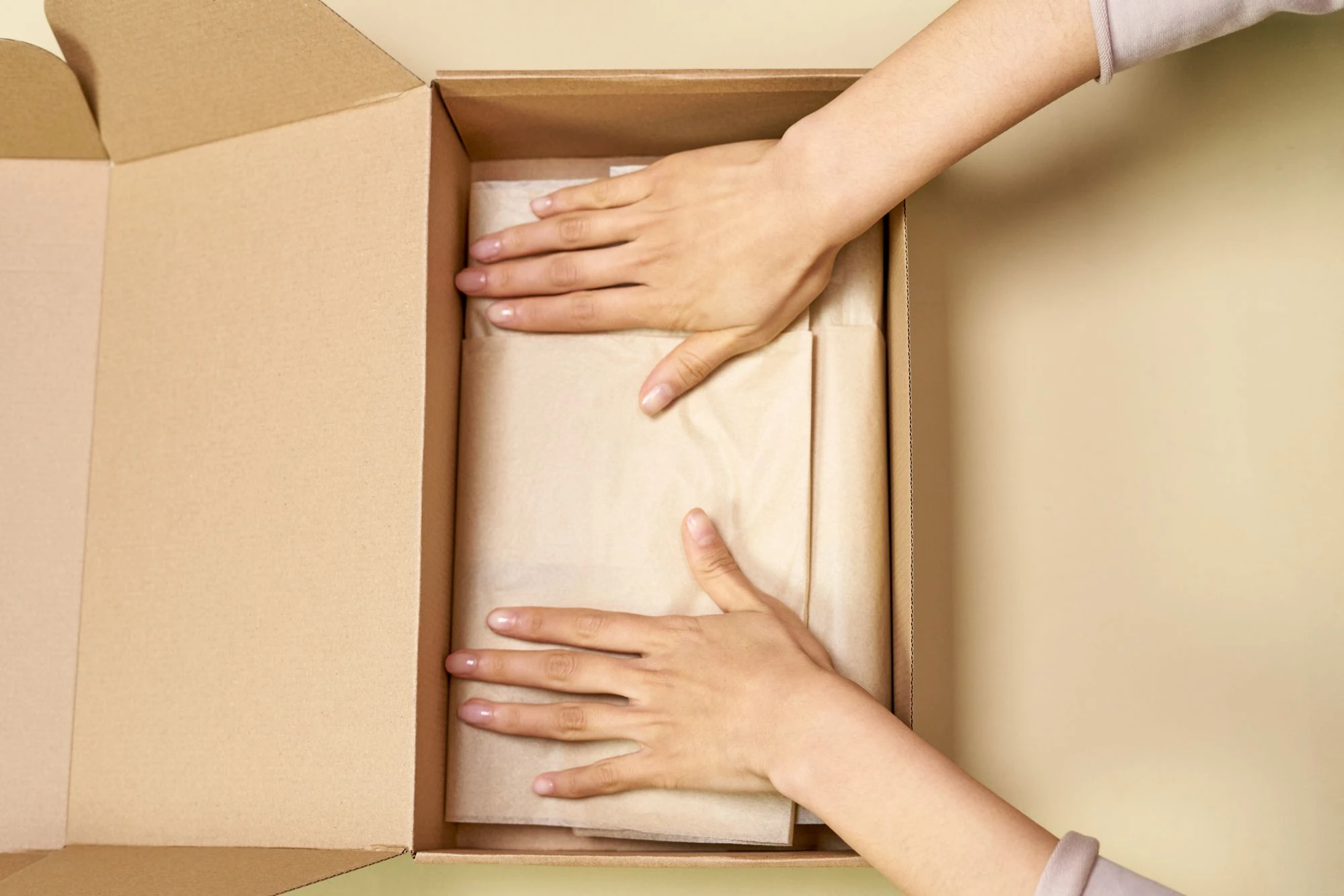 Hands arranging protective paper inside a cardboard mailer