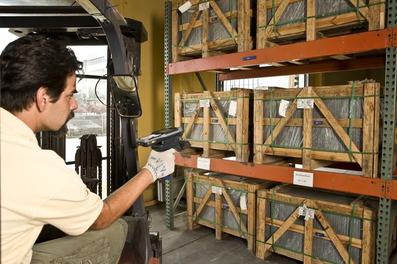 Warehouse operator using a handheld reader beside racks of crated goods