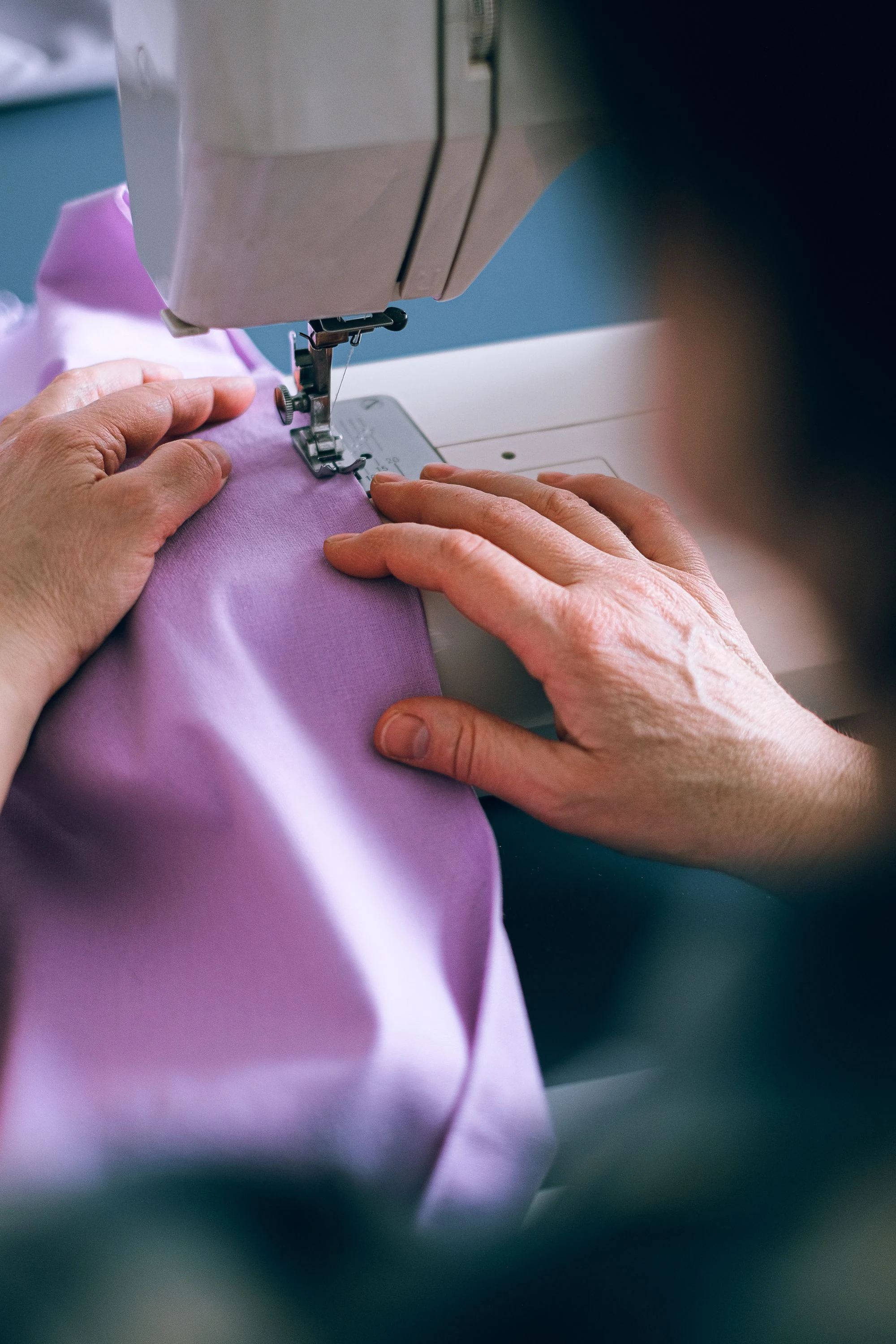 Hands guiding purple fabric through a sewing machine
